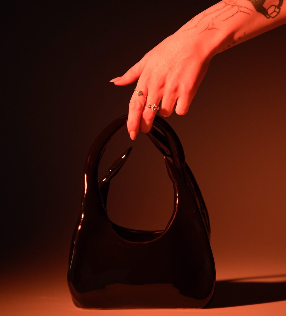 Black glazed ceramic handbag, with a hand grazing the handle to communicate scale